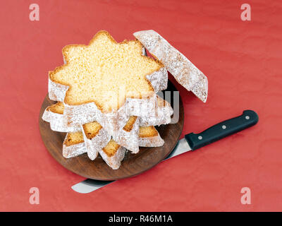 In Scheiben geschnitten Pandoro, süßen italienischen Hefe Brot, traditionelle Weihnachten behandeln. Mit Messer auf Rot. Overhead flach anzeigen. Stockfoto