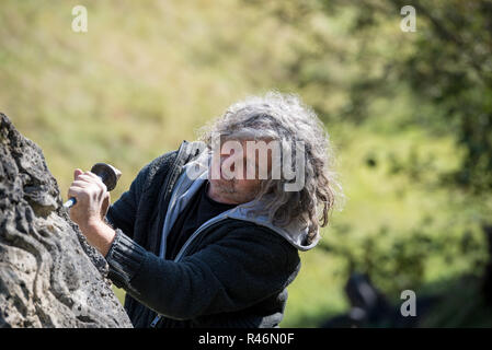 Senior Bildhauer Carving in großen Stein eine Skulptur außerhalb an einem sonnigen Tag. Stockfoto