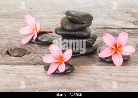 Plumeria Blumen und schwarze Steine auf verwittertes Holz Hintergrund Stockfoto