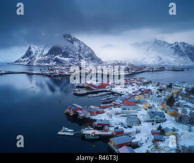 Luftaufnahme von Reine in bewölkten Tag im Winter auf den Lofoten Inseln, Norwegen. Moody Landschaft mit blaues Meer, schneebedeckte Berge in Wolken, Felsen, Villag Stockfoto