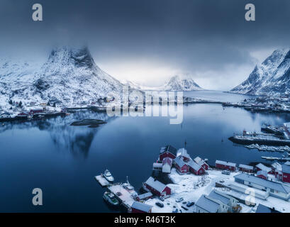 Luftaufnahme von Reine in bewölkten Tag im Winter auf den Lofoten Inseln, Norwegen. Moody Landschaft mit blaues Meer, schneebedeckte Berge in Wolken, Felsen, Villag Stockfoto