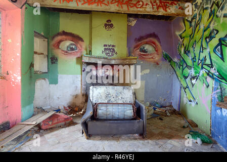Graffiti an den Wänden ist Müll übersäte Böden und gebrochene Sofa in die Hocke, Interieur des verlassenen Haus Frankreich Stockfoto