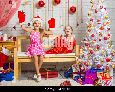 Auf der Bank sitzt ein Mädchen in eine Mütze und Handschuhe von Santa Claus, das andere Mädchen mit einem Lachen kommt aus dem Beutel Stockfoto