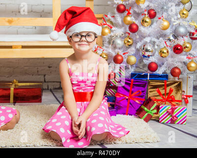 Mädchen, die in der Red Hat und die lustige Runde Gläser sitzt auf der Matte an der Weihnachtsbäume Stockfoto