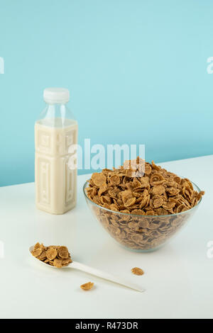 Helathy vegetarisches Frühstück Mahlzeit Konzept. Schüssel voller Getreide und eine Flasche Milch auf Weißem und Blauem Hintergrund Stockfoto