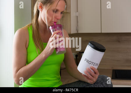 Kaukasische Frau in der Turnhalle Anzug trinken Protein Shake in der Küche Stockfoto