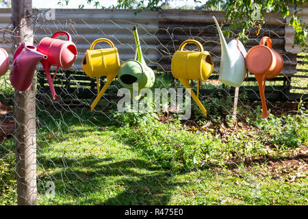 Bunte giesskannen am Zaun im Garten an einem sonnigen Tag. Stockfoto