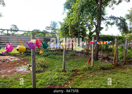 Bunte giesskannen am Zaun im Garten an einem sonnigen Tag. Stockfoto