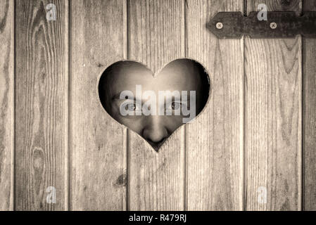 Holz- Außen-WC mit Herz an der Tür. Ein Mann geht durch eine herzförmige Fenster. Stockfoto