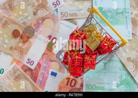 Miniatur Einkaufswagen mit Geschenken und europäisches Geld als Symbol für Urlaub Aufwendungen Stockfoto