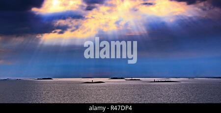 Die Sonne hinter den Wolken mit Lichtstrahlen nach unten scheint auf das Meer Stockfoto