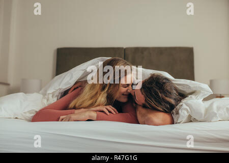 Paar auf dem Bett zu Hause liegen romancing durch Berühren der Nase. Glücklich der Mann und die Frau auf dem Bett in einer gemütlichen Decke Ausgabe Zeit fallen zusammen liegen. Stockfoto