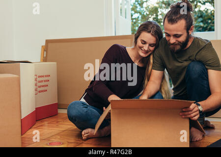 Paar nach dem Umzug in ein neues Zuhause ihre Sachen auspacken. Paar zusammen sitzen auf dem Boden auspacken ihre Boxen. Stockfoto