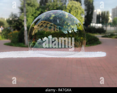 Große Seifenblase auf eine Blase Gebläse. Gebäude und Bäume in einer riesigen Blase in einem Stadtpark zu reflektieren. Stockfoto