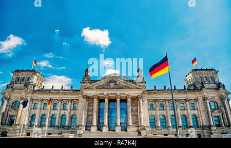 Deutsche Fahnen im Wind am berühmten Reichstag, Sitz des deutschen Parlaments (Deutscher Bundestag), an einem sonnigen Tag mit blauen Himmel und Cl Stockfoto