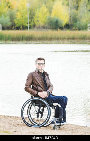 Junge Mann sitzt im Rollstuhl durch den See. Stockfoto
