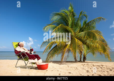 Santa Claus sitzt im Liegestuhl am Strand. Stockfoto