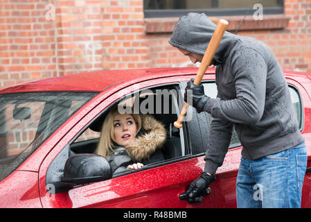 Räuber mit Baseballschläger, während Sie Frau im Auto. Stockfoto