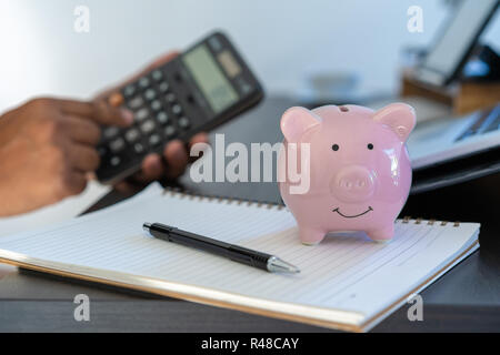 Sparschwein und Rechner auf dem Schreibtisch Business Document Taschenrechner zählen Geld Stockfoto