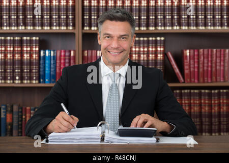 Buchhalter Schreiben auf Dokument während der Verwendung von Taschenrechner am Tisch Stockfoto