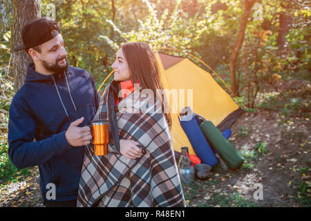Schönes Bild von junges Paar am Zelt und an jedem anderen suchen. Sie ist mit der Decke zugedeckt. Kerl hält thermotasse. Menschen sind ruhig und glücklich. Stockfoto