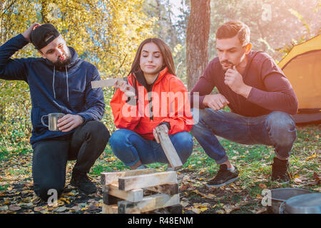 Drei Freunde sitzen in squad Position und Blick auf brickets aus Holz. Junge Frau, die ein Stück von ihm. Sie wissen nicht, was mit ihm zu tun. Die Leute sind frustriert. Stockfoto