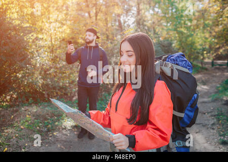 Bild von zuversichtlich und fröhliche junge Frau mit bakcpack. Sie hält Karte und es betrachtet. Junge Mann hinter versuchen Signal am Telefon zu erwischen. Er hält ihn auf. Stockfoto
