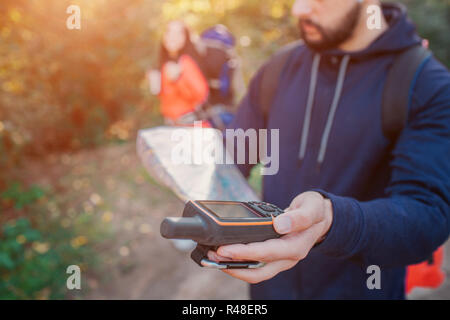 Bild junger bärtiger Mann mit Sat-Telefon in der Hand. Es gibt Karte in eine andere Hand. Junge Frau hinter ihm. Sie hat Rucksack. Stockfoto