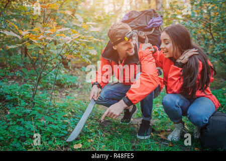 Glückliches Paar in der Gruppe Position im grünen Wald sitzen. Sie fanden Pilz. Kerl hält Machete in der Hand. Er verweist auf Pilz. Junge Frau glücklich ist. Stockfoto