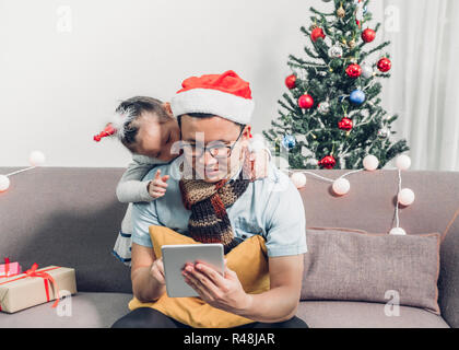Vater und Tochter sitzen auf dem Sofa und wählen Sie Weihnachtsgeschenk und Einkaufen von Online Store von Tablette Xmas Party, Urlaub Geschenk, das festliche Stockfoto