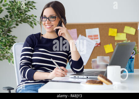 Selbstbewussten jungen Frau arbeitet sie in ihrem Büro mit Handy. Stockfoto