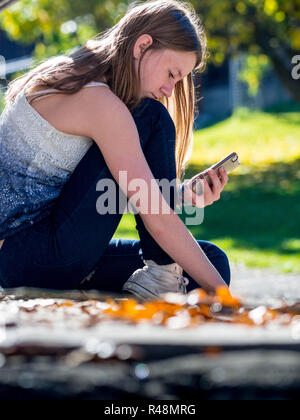 Teenager-Mädchen liest ihr Handy in der Sonne Stockfoto