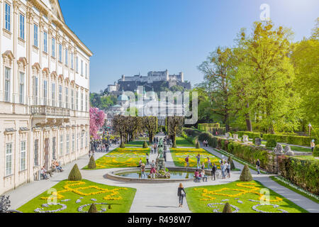 Touristen zu Fuß durch die berühmten Mirabellgarten mit berühmten Festung Hohensalzburg im Hintergrund an einem sonnigen Tag mit blauen Himmel und Wolken in Summe Stockfoto