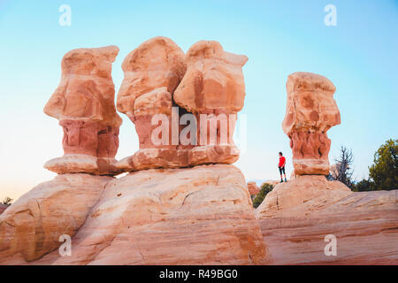 Schöne Sicht der männlichen Wanderer stehen zwischen erstaunliche Vier Hoodoos Sandstein Felsformationen in Devil's Garten im schönen Abendlicht bei Sonnenuntergang, Grand Stockfoto