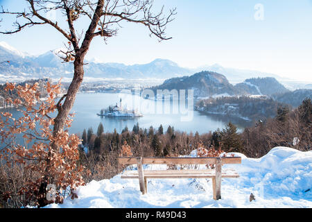 Wunderschöne Aussicht auf Holzbank mit Blick auf den berühmten Bleder See mit Insel und von Julischen Alpen im Hintergrund bei Sonnenaufgang im Winter, Slowenien Stockfoto