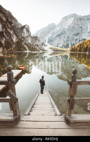 Wunderschöne Aussicht auf einen jungen Mann stehen auf hölzernen Treppen den Sonnenaufgang an der berühmten Lago di Braies Dolomiten, Südtirol, Italien Stockfoto