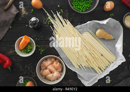 Zutaten zum Kochen udon Nudeln mit Hühnerfleisch auf dunklen Holztisch in der Küche zu Hause Top View Stockfoto