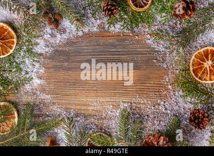 Weihnachten Rahmen aus Tannenzweigen, Tannenzapfen und getrocknete Orangenscheiben auf verschneiten Holztisch Stockfoto