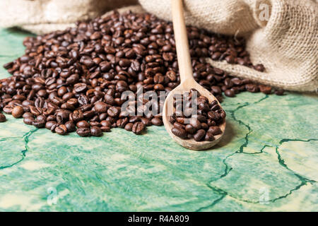 Kaffeebohnen in Kaffee sackleinen Beutel auf grüne Fläche und Löffel aus Holz mit Kaffeebohnen auf der Oberseite. Stockfoto