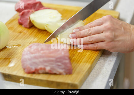 Frau Schneidet Zwiebeln und rohes Fleisch auf einem Holzbrett Stockfoto