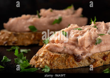 Zwei Scheiben Brot mit Gemüse Pastete und gehackte grüne Petersilie auf dunklem Schiefer, Ansicht schließen Stockfoto