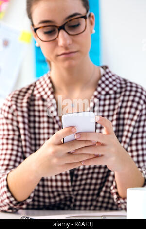 Schöne junge Frau mit ihrem Handy im Büro. Stockfoto