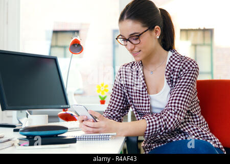 Schöne junge Frau mit ihrem Handy im Büro. Stockfoto