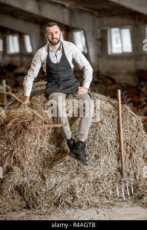 Porträt einer stattlichen Bauer in Schürze sitzt auf dem Heu im Stall auf dem Ziegenhof Stockfoto