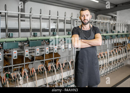 Porträt einer männlichen Arbeitnehmer in schwarzer Uniform auf dem Ziegenhof mit melken Linie auf dem Hintergrund Stockfoto