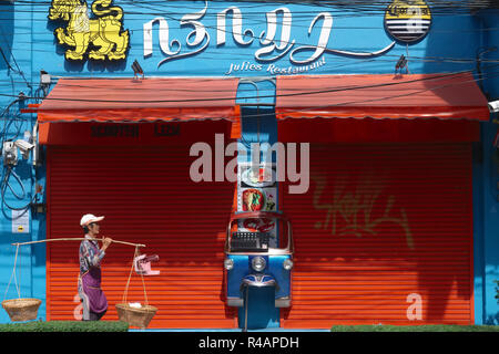 Ein Anbieter mit Schulter- Körbe vorbei an einem Restaurant, vorne geschmückt mit Teil eines Tuk-tuk, einem Dreirädrigen Art Taxi; Bangkok, Thailand Stockfoto