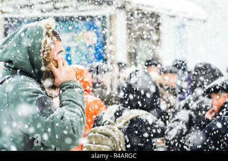 Der Mensch in der Motorhaube Telefonieren während eines Schneesturms. In einem städtischen Umfeld Blizzard. Menschen auf der Bushaltestelle in Schneefall. Winter Wetter Hintergrund Stockfoto