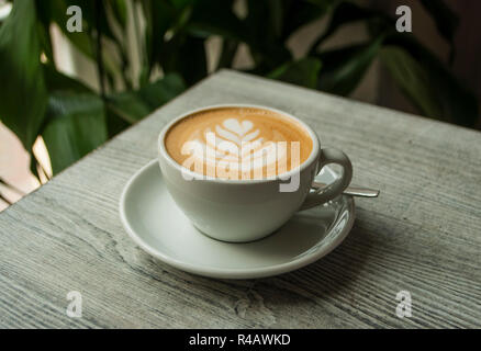 Eine Tasse Kaffee mit schönen Latte Art auf einem grauen hölzernen Tisch in einem Cafe. Stockfoto