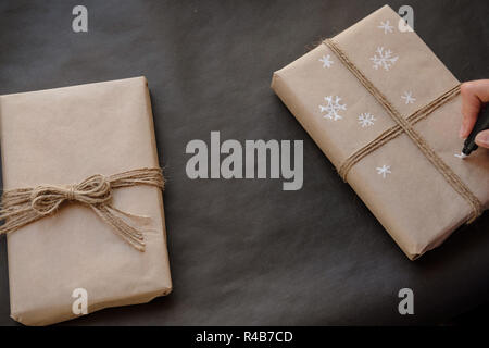 Frau Zeichnung auf Papier Schneeflocken Paket Weihnachten, Geschenk auf schwarzem Hintergrund. Weibliche Hände malen auf Geschenke für Winterurlaub. Weihnachten, Ne Stockfoto