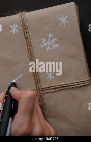 Frau Zeichnung auf Papier Schneeflocken Paket Weihnachten, Geschenk auf schwarzem Hintergrund. Weibliche Hände malen auf Geschenke für Winterurlaub. Weihnachten, Ne Stockfoto